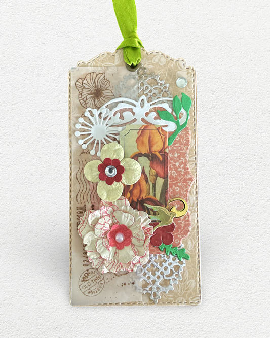 A decorative gift tag with a floral hand-embossed design, featuring various colored flowers and foliage on a white background, attached with a satin ribbon.
