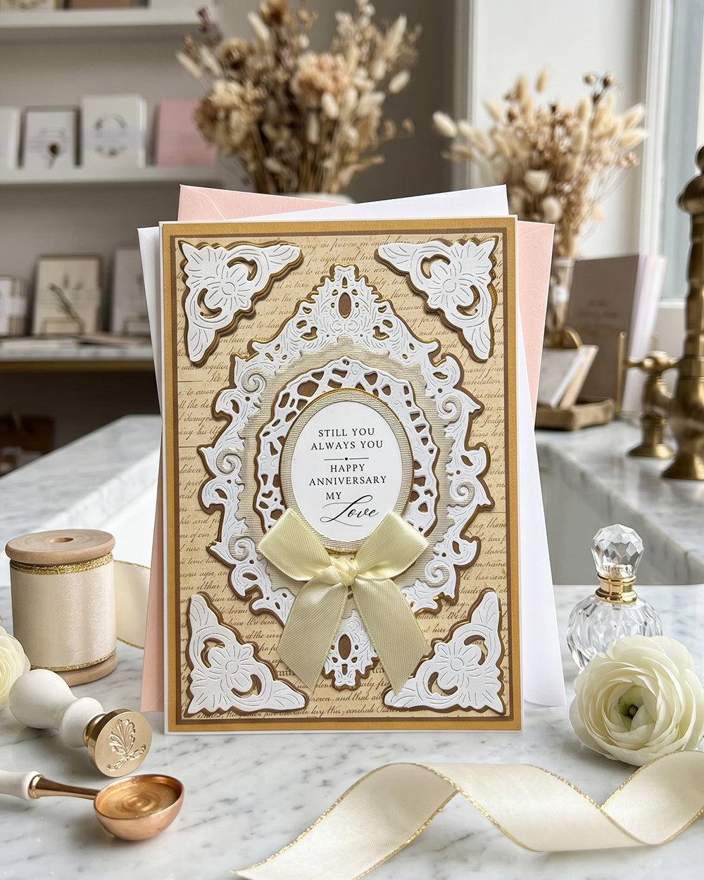 Handmade anniversary card in gold and white. An ornate white embossed die-cut frame with floral corners and lacework detail sits over an antique script background in warm gold. A layered oval cameo at the centre reads "Still you. Always you. Happy Anniversary my Love" in elegant typography, made in New Zealand by Del Cards.