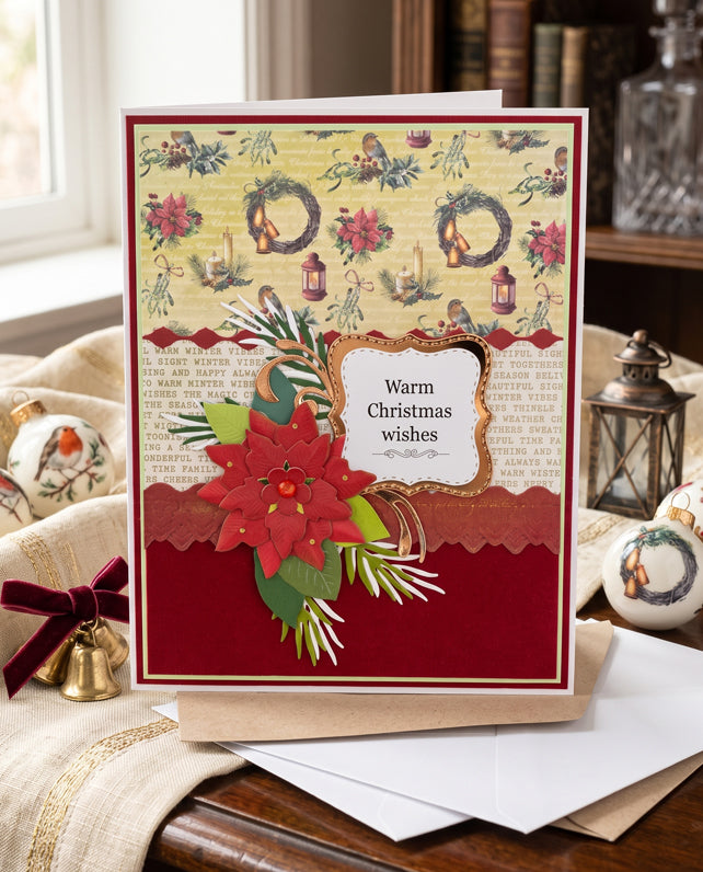 A handmade Christmas greeting card displayed on a table with a kraft envelope. The card features a vintage collage design with wreaths, birds, and a large red poinsettia on a deep red lower section.