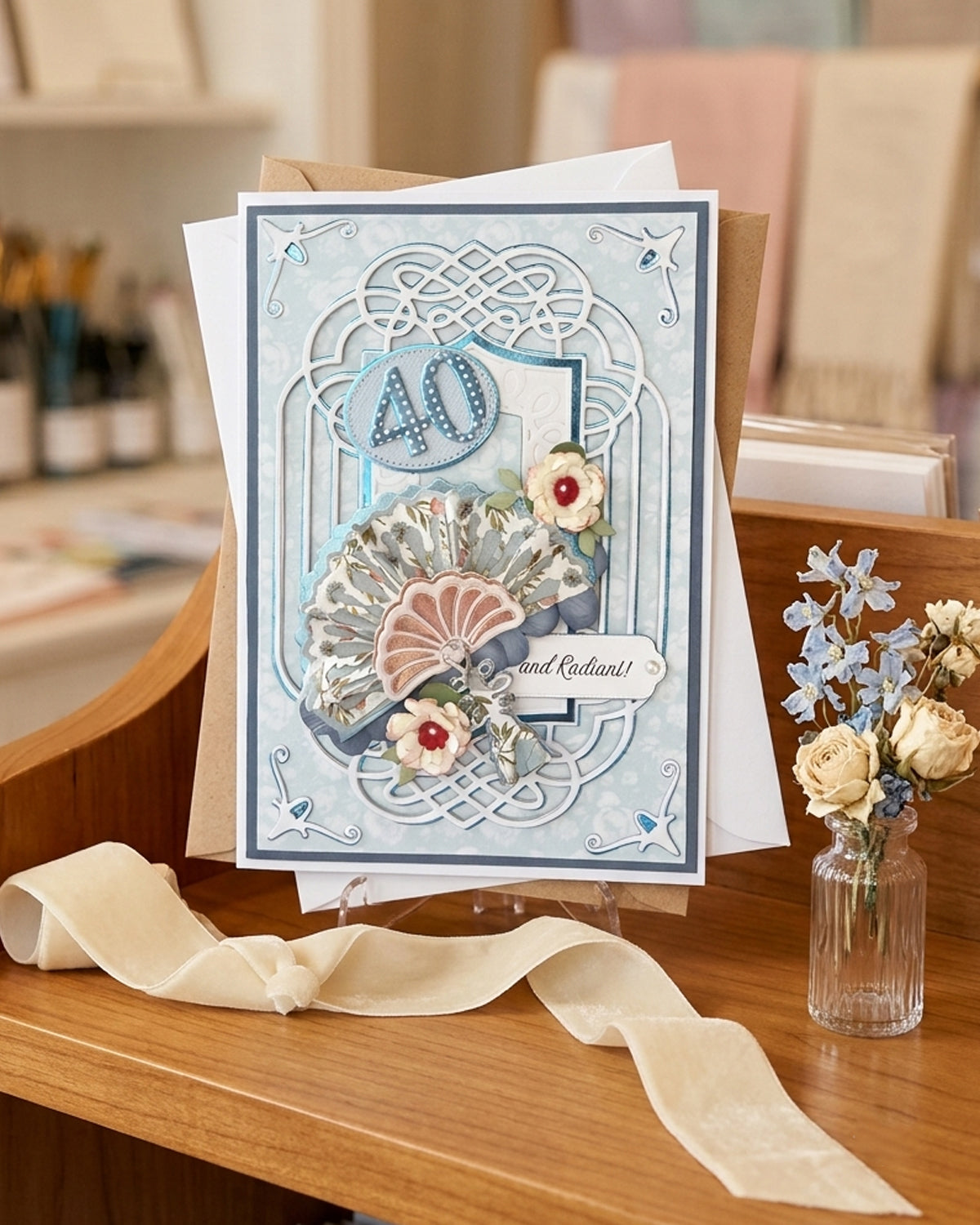 Handmade 40th birthday card displayed upright on a wooden surface beside dried flowers and ribbon, styled in a softly lit interior setting, made by Del Cards.