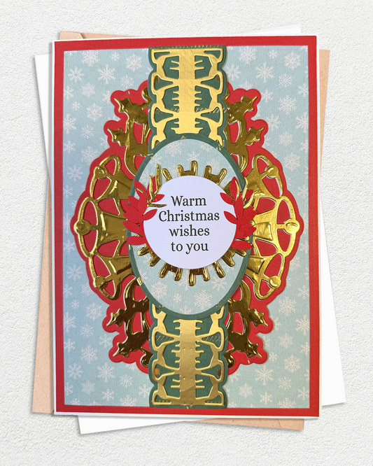 A handmade Christmas greeting card with a red border, gold and red ornate cutout design, and a light blue snowflake-patterned background. The center features a white oval with the text 'Warm Christmas wishes to you'.