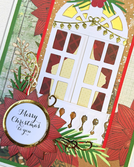 A close-up of a handmade Christmas card featuring a white arched window with red and gold patterned panes, surrounded by red poinsettias, green pine branches, gold ornaments, and a round white tag that reads 'Merry Christmas to you'.