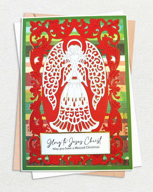A layered Christmas greeting card featuring a white angel silhouette cutout over a red ornate border, with a green striped background and a white message panel reading 'Glow to Jesus Christ May you have a Blessed Christmas.' The card is photographed on top of white envelopes against a light textured wall.
