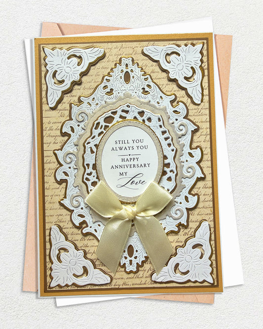 Handmade anniversary card in gold and white. An ornate white embossed die-cut frame with floral corners and lacework detail sits over an antique script background in warm gold. A layered oval cameo at the centre reads "Still you. Always you. Happy Anniversary my Love" 