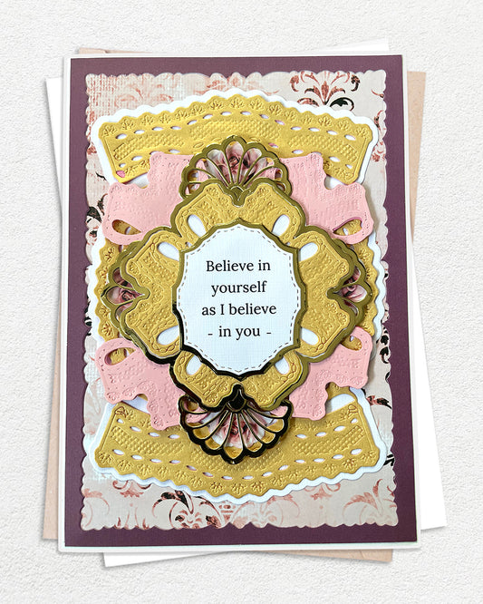 Handmade luxury encouragement card on a deep plum cardstock base, layered with blush pink and antique gold die-cut panels in graduating scalloped and ornate shapes. A large gold embossed decorative frame with fan shell detail at the base centres a white sentiment panel reading "Believe in yourself as I believe in you" in fine print. Floral patterned paper peeks through the layered die-cuts adding delicate detail. White envelope visible beneath. Handmade luxury card made in New Zealand.
