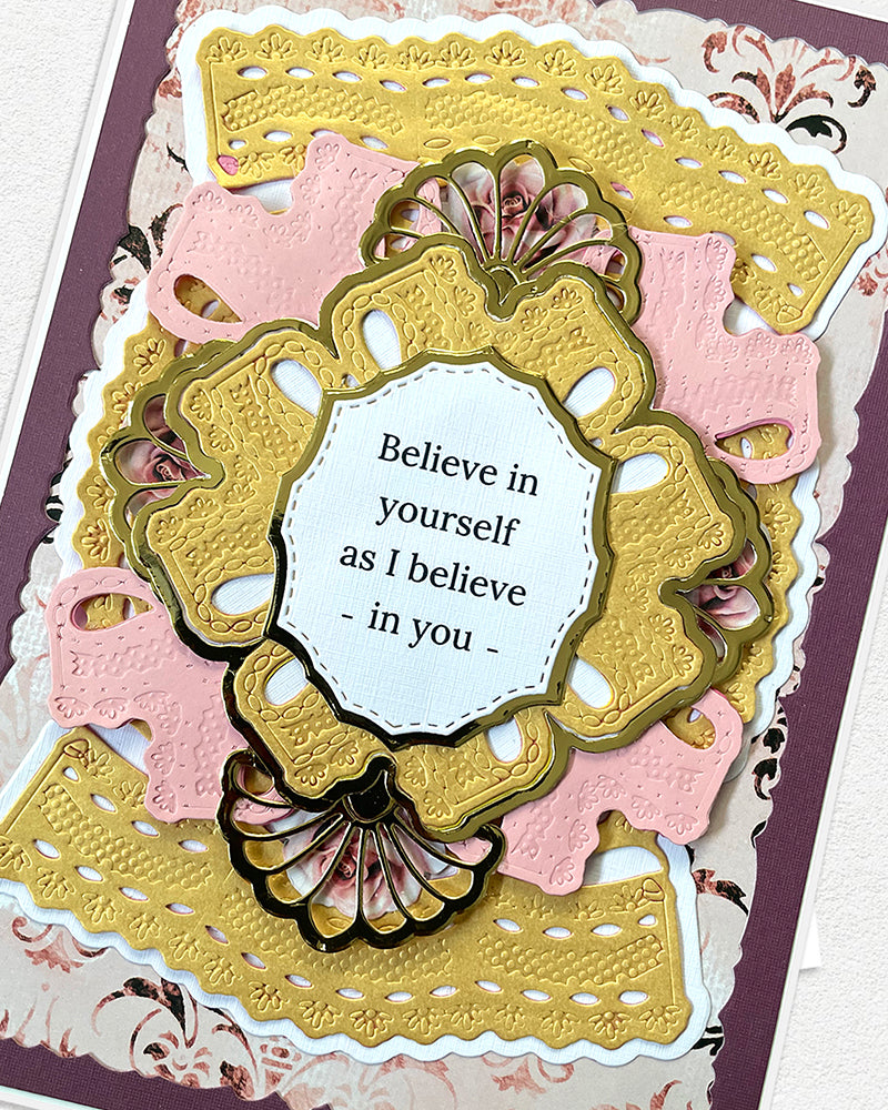 Full front view of a handmade plum, blush and gold greeting card featuring layered ornate die-cut panels, a gold embossed centrepiece frame with fan shell detail, and the sentiment "Believe in yourself as I believe in you." A heartfelt handmade encouragement or birthday card made in New Zealand by Del Cards.
