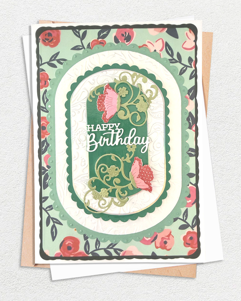 Handmade Happy Birthday card with layered emerald and cream scalloped frames, floral vine die-cuts and pink poppy blooms, on a forest green floral background with envelopes, made by Del Cards NZ
