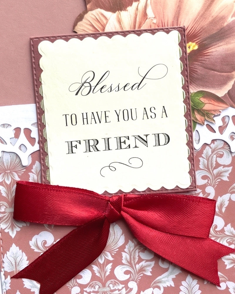 Full front view of a handmade friendship card featuring vintage peach paper peonies on a dusty rose panel, white damask lower panel, deep red satin ribbon bow and a cream sentiment tag reading "Blessed to have you as a friend". A warm, heartfelt handmade friendship card made in New Zealand,  perfect for birthdays, appreciation or simply celebrating a cherished friend.