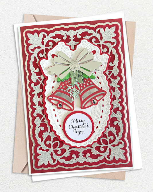 A handmade Christmas greeting card with intricate red and white laser-cut floral borders, featuring two red bells, a beige bow, green leaves, and a round white label that reads 'Merry Christmas to you'. The card is displayed on top of a kraft envelope against a textured off-white background.