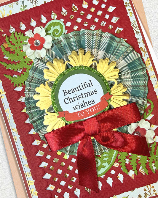A close-up of a handmade Christmas greeting card featuring a red lattice border, a green and gold plaid rosette, a red ribbon bow, and a central round label that reads 'Beautiful Christmas wishes TO YOU!'.