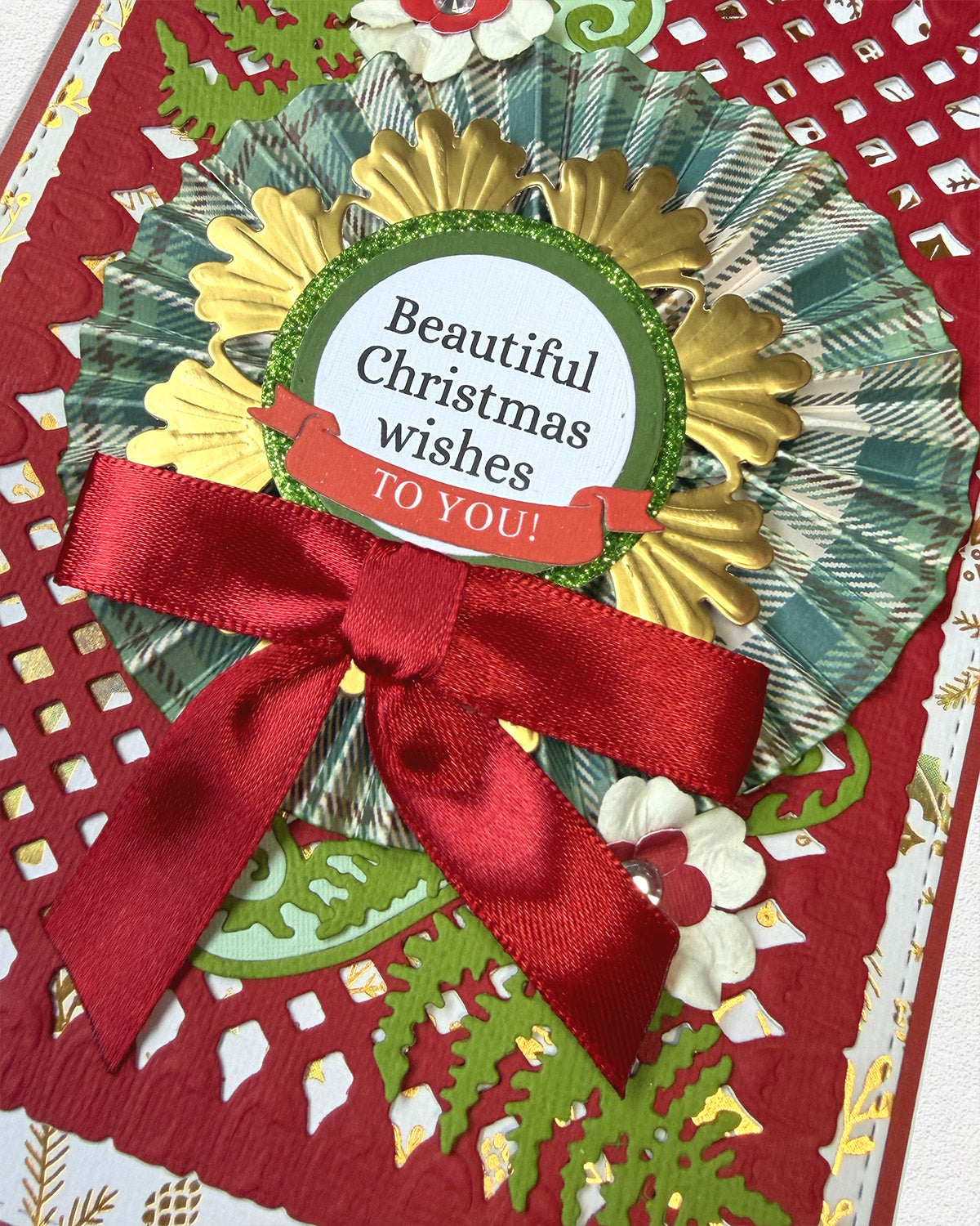A close-up of a handmade Christmas greeting card featuring a red satin bow, gold and green plaid fan accents, and a central round label that reads 'Beautiful Christmas wishes TO YOU!'.