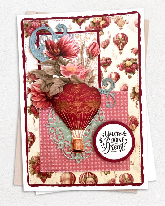 Handmade luxury encouragement card featuring a vintage floral patterned background with small hot air balloon illustrations in deep red and teal. A pink gingham centre panel is layered over the base, topped with a large hand-applied dimensional red and gold vintage hot air balloon with basket detail. A large deep pink dahlia and green leaves spill from the upper left, with a teal decorative scroll accent. A circular sentiment tag reads "You're doing Great" in bold and script lettering. 