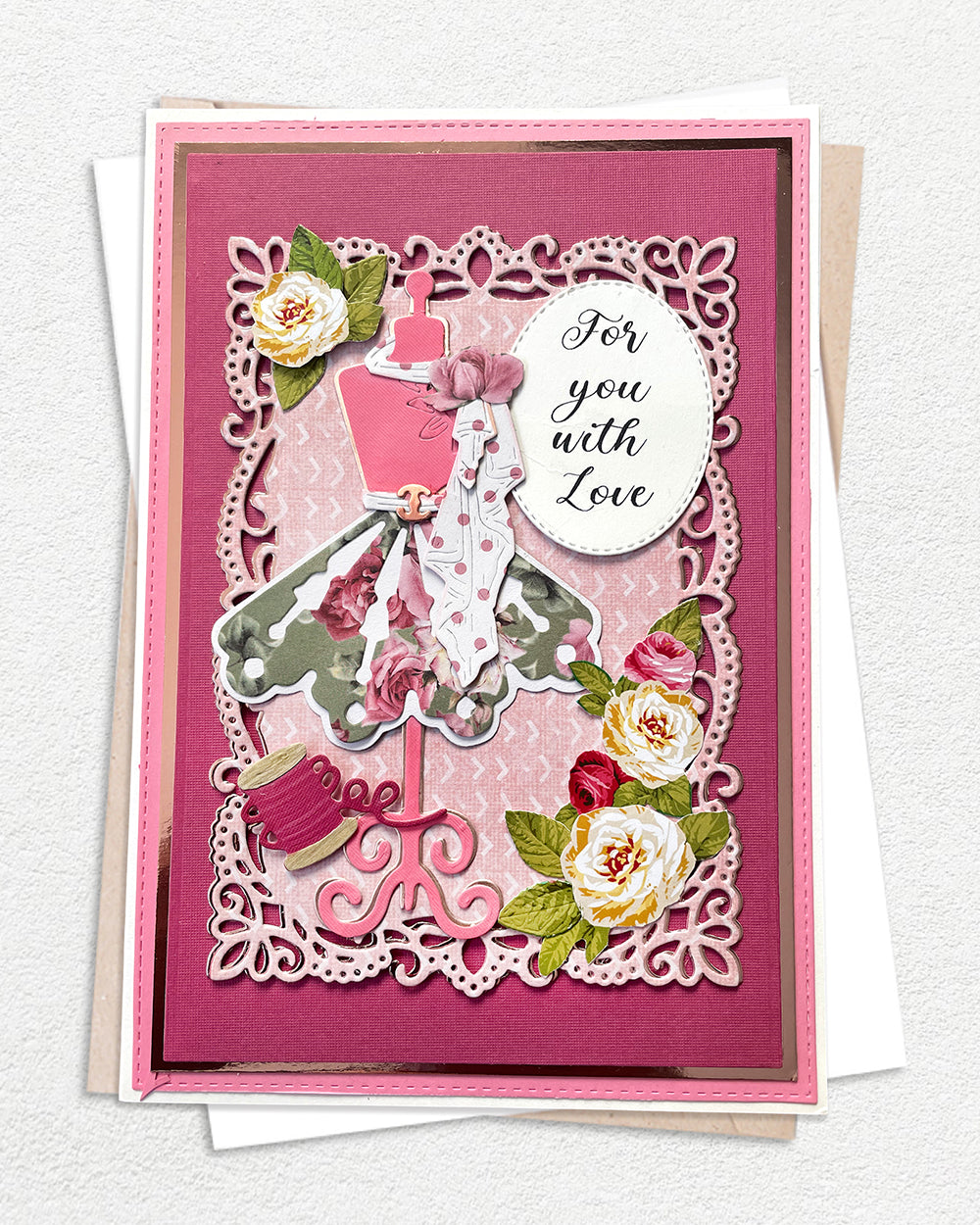 Handmade luxury greeting card on a deep rose pink cardstock base with an ornate white lace-style die-cut border frame. A central elegant lady figure in a sweeping grey and white ball gown with pink accents stands tall, surrounded by hand-applied cream and pink paper roses with green leaves. A circular sentiment tag reads "For you with Love" in flowing script. Decorative pink scroll flourishes at the base add a finishing detail. White envelope visible beneath. Handmade luxury card made in New Zealand.