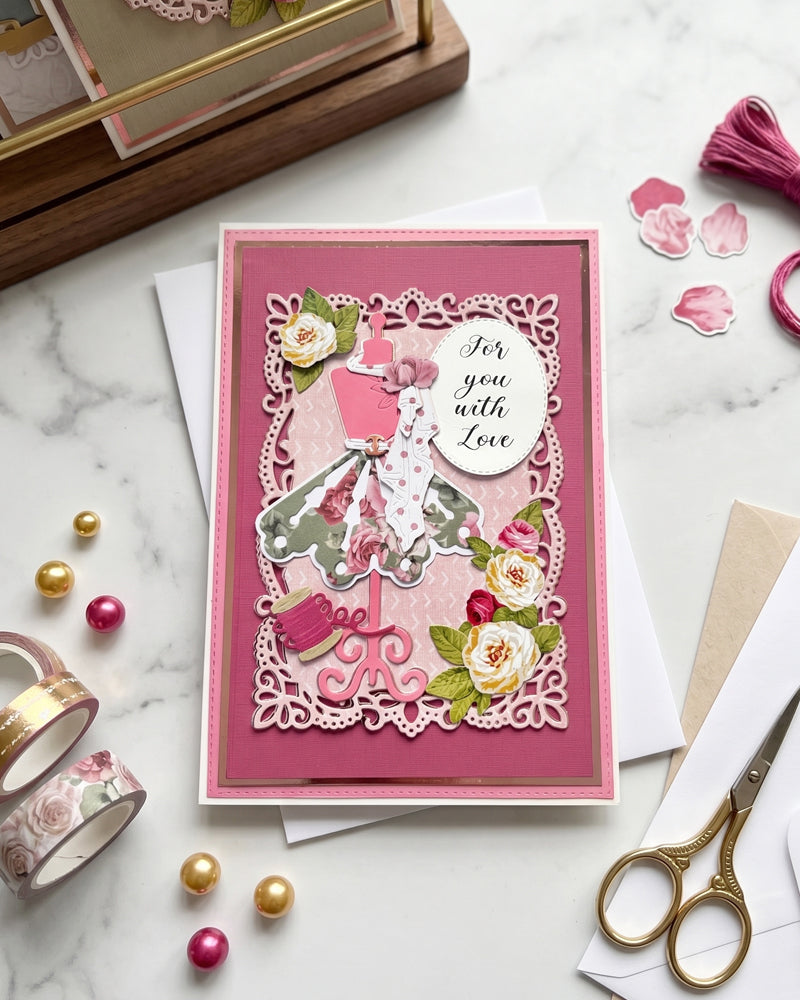 Handmade "For you with Love" card displayed upright in a styled flat-lay setting with gold scissors, pearl beads and pink tassel props alongside. Deep rose pink with an elegant ball gown figure and cream florals make this a strikingly feminine handmade card made in New Zealand by Del Cards NZ.