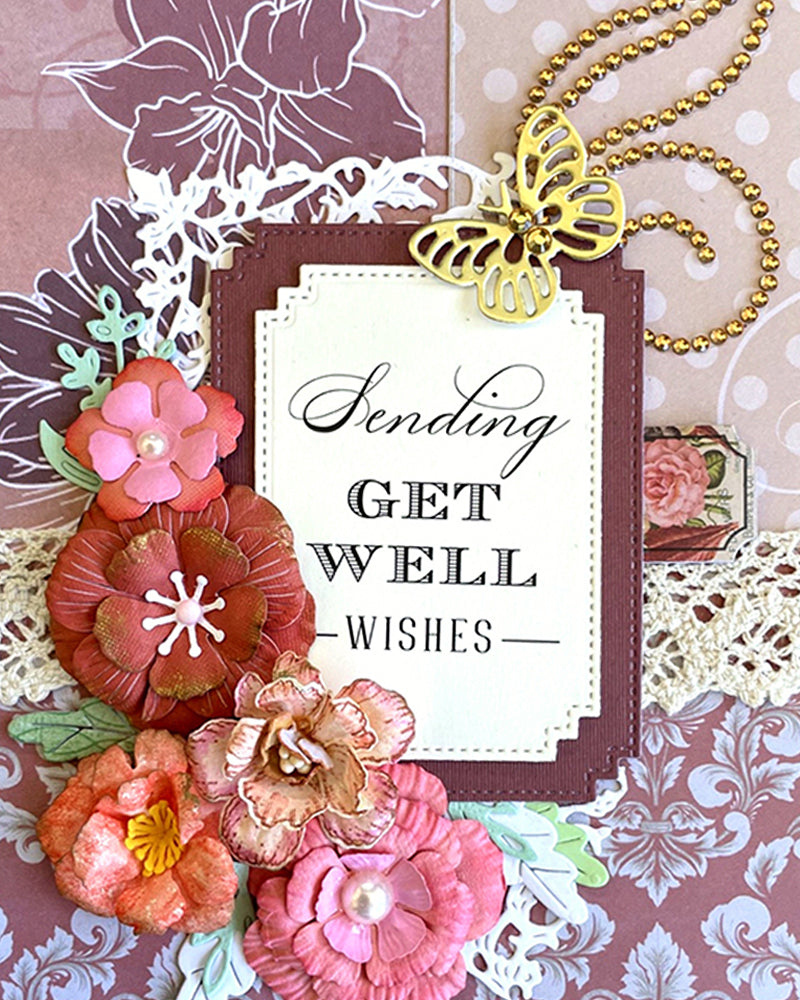 Full front view of a handmade burgundy and mauve get well card featuring a large-scale floral stamped background, white lace border panel, gold swirl flourish, clustered rose and coral paper flowers and a "Sending Get Well wishes" sentiment frame. A warm, sophisticated handmade get well card made in New Zealand by Del Cards NZ.