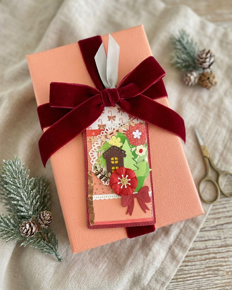 Luxury handmade Christmas gift tag styled on a coral wrapped gift with burgundy velvet bow and winter foliage — Del Cards NZ handmade gift tags add a festive handcrafted touch to any Christmas present