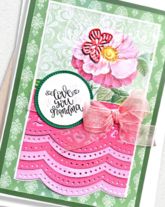 Detail of a handmade grandma card showing a large layered pink peony paper flower with red centre detail against a sage green damask background, with the top of a circular "I love you Grandma" sentiment tag visible below. Handmade greeting card made in New Zealand.

