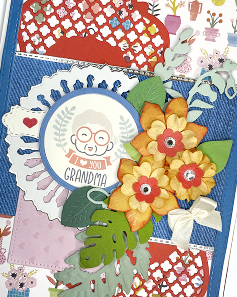Full front view of a bright handmade card for grandma featuring cobalt blue cardstock, colourful patchwork-style illustrated paper, white doily die-cut framing, bold yellow paper daisies and a charming illustrated owl sentiment circle. A cheerful, unique grandmother card handmade in New Zealand.