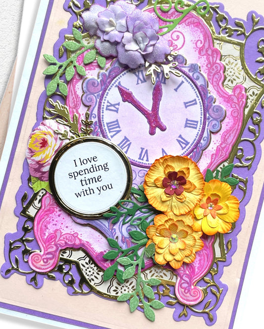 Close-up of handmade card showing ornate purple clock face, layered yellow and pink die-cut flowers, and decorative purple frame detail