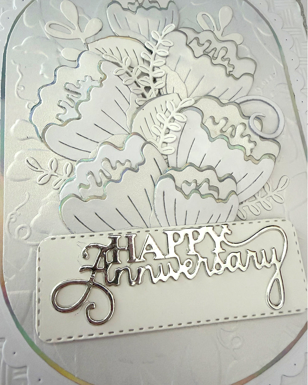 Close-up of layered die-cut flowers with silver foil outlines on white anniversary card