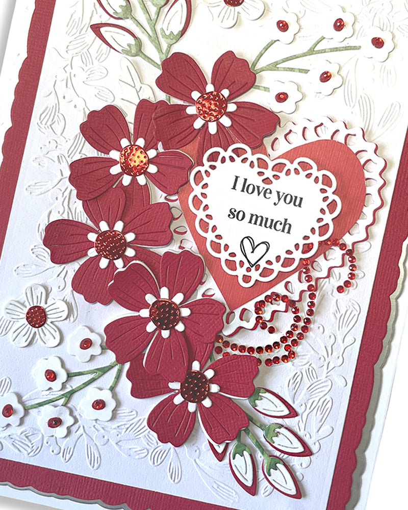 Close-up of handmade love card showing dimensional deep red die-cut flowers with jewel centres and delicate foliage detail on embossed white background