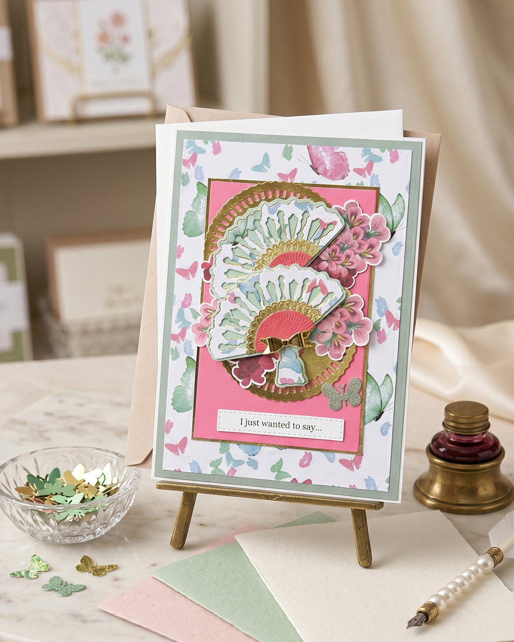 Handmade mint and pink "I just wanted to say" card displayed upright on a small wooden easel in a soft styled setting with an ink bottle and greenery alongside. Fresh mint, gold and hot pink tones make this a charming handmade greeting card made in New Zealand by Del Cards NZ.