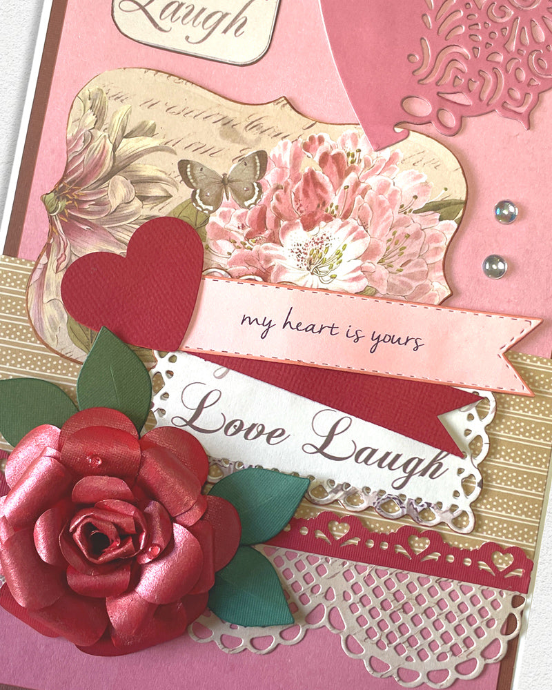 Close-up of handmade love card showing vintage cameo and floral imagery, red heart die-cut, and layered pink and gold decorative panels