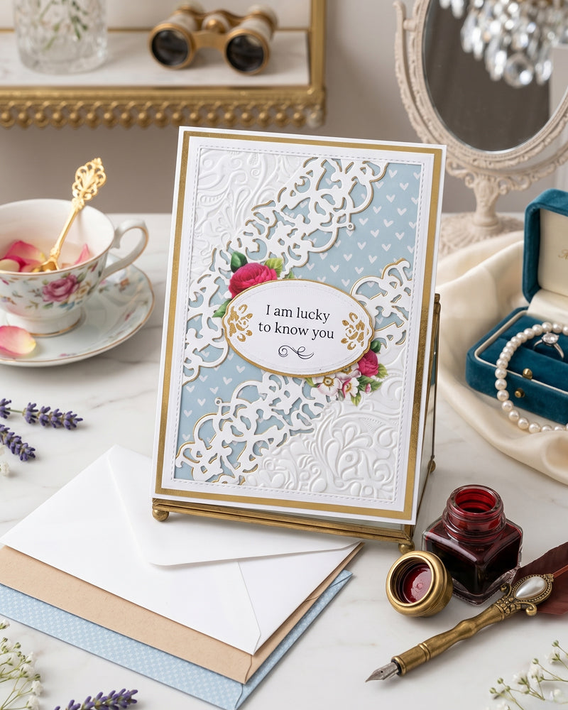 Handmade powder blue and white "I am lucky to know you" friendship card displayed flat in a styled setting with a teacup, ink pen, candle and soft props alongside. Delicate white lace overlay and gold detailing make this a graceful handmade card made in New Zealand by Del Cards NZ.
