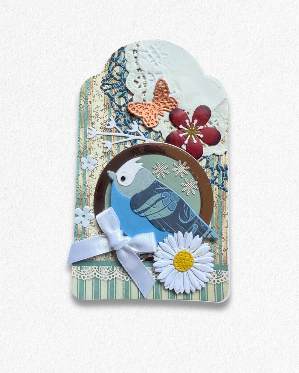 Handmade mini card by Del Cards NZ featuring a blue bird, white bow, and daisy on a striped background.