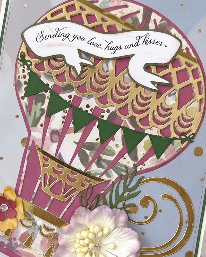 Close-up of handmade card showing dimensional hot air balloon in deep pink and gold geometric pattern with bunting flag detail and sentiment banner