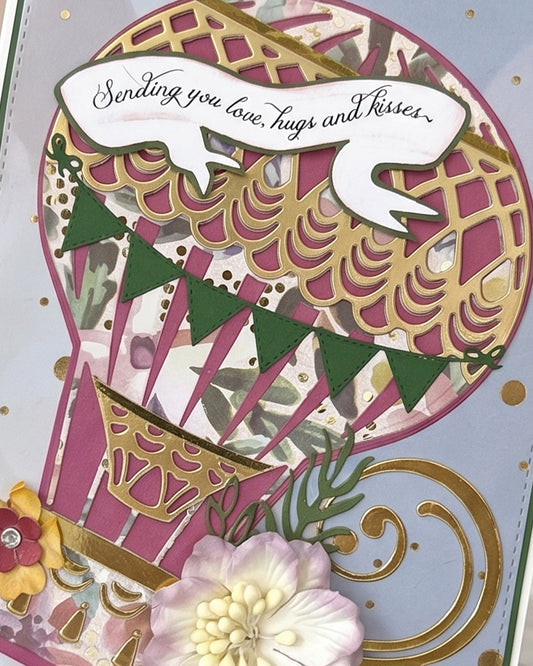 Close-up of handmade card showing dimensional hot air balloon in deep pink and gold geometric pattern with bunting flag detail and sentiment banner