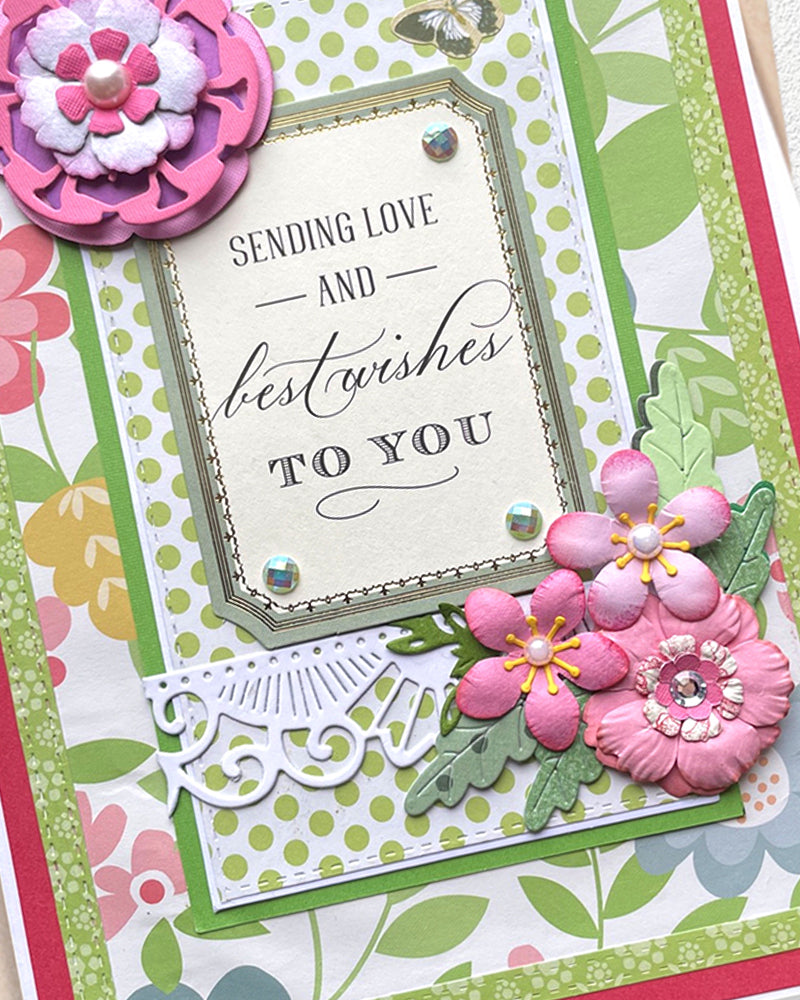Greeting card with floral decorations and text 'Sending love and best wishes to you' on a colorful background. Made in NZ by Del Cards.