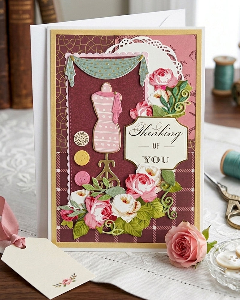 Amazing Thinking of You card with dressmaker's mannequin detail displayed upright in a soft styled setting with stationery props alongside. Rich plum, gold and pink tones with a charming craft-inspired design make this a distinctive handmade greeting card made in New Zealand by Del Cards.

