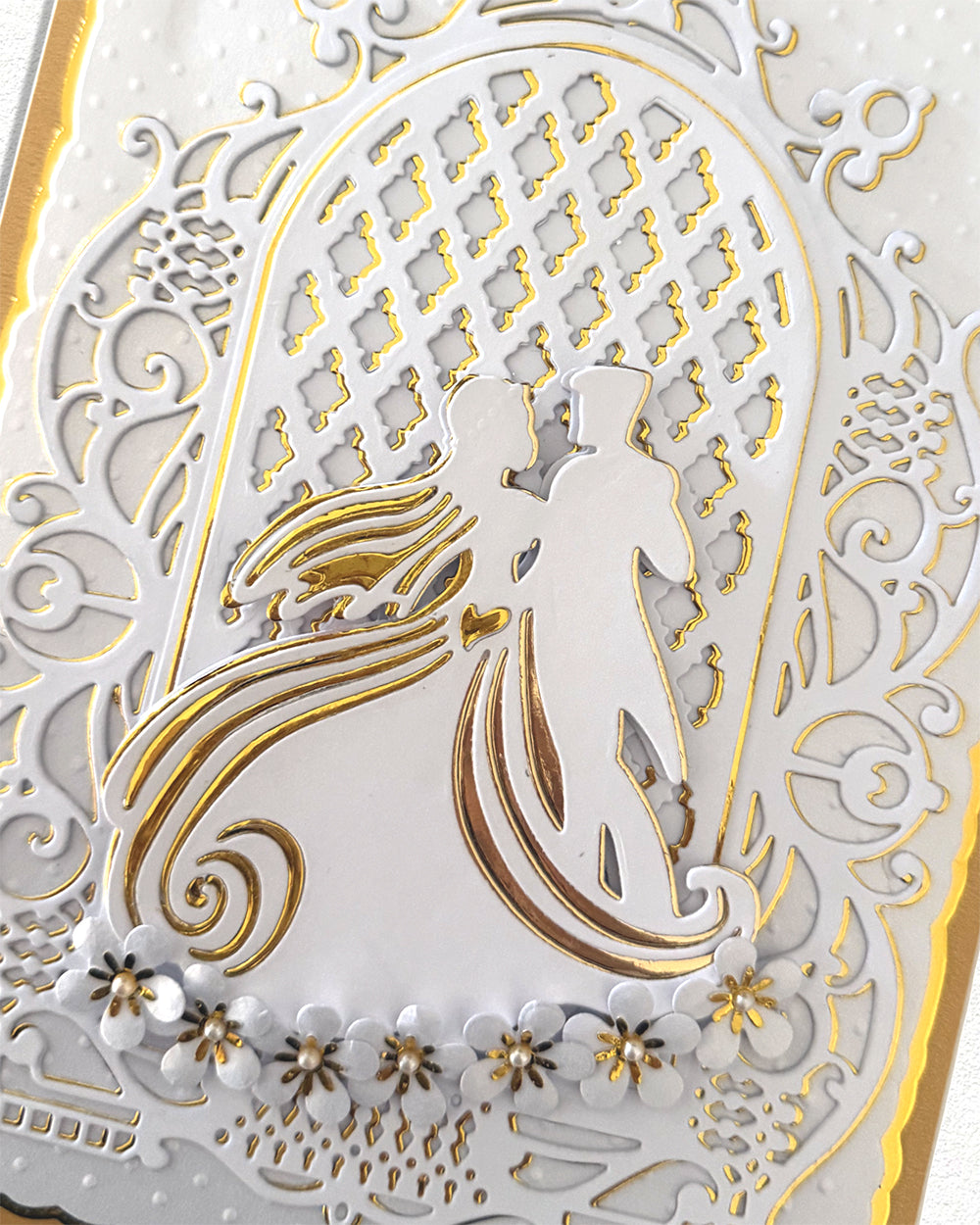 Close-up of hand-finished wedding card showing gold foil bride and groom silhouette with pearl floral detailing
