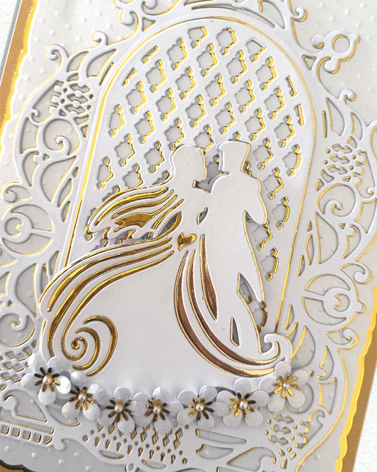 Close-up of hand-finished wedding card showing gold foil bride and groom silhouette with pearl floral detailing
