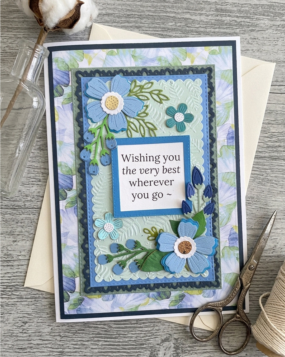 A handmade layered card with floral embellishments and the text 'Wishing you the very best wherever you go', made by Del Cards NZ.