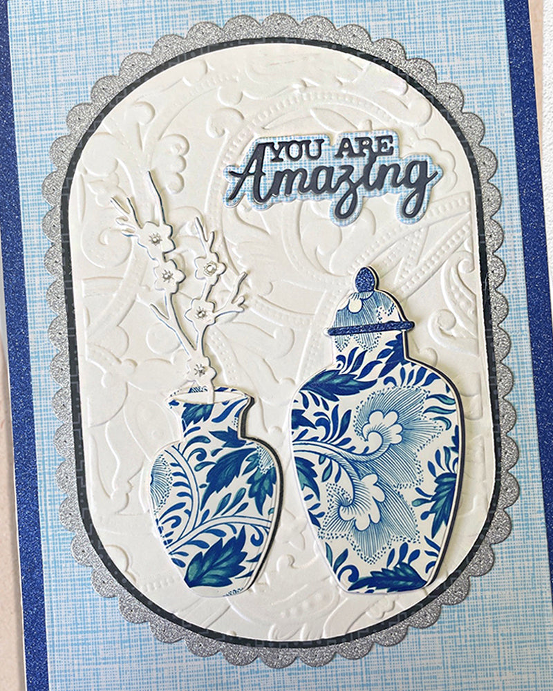Front view of a handmade navy and ivory greeting card featuring a silver-edged scalloped oval centrepiece with chinoiserie ginger jar illustrations, hand-embossed detailing and "YOU ARE Amazing" sentiment. An elegant, unique handmade card made in New Zealand — perfect for birthdays, appreciation or milestone occasions.