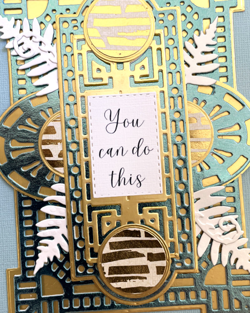 Close-up of a handmade luxury card showing the upper portion of an intricate gold Art Deco geometric die-cut frame with a circular gold element at the top, white silver fern fronds on either side, and a blush sentiment tag reading "You can do this." Sage green and steel blue layered background. Handmade greeting card made in New Zealand.