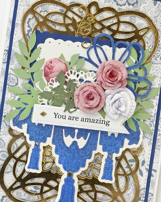 Full front view of an ornate handmade greeting card featuring a gold and black swirling filigree frame, cobalt blue glitter centre panel, blue chandelier die-cut, and cascading pink and white paper roses. Sentiment reads "You are amazing." A lavish, one-of-a-kind handmade card made in New Zealand — ideal for birthdays, milestones or someone truly deserving.
